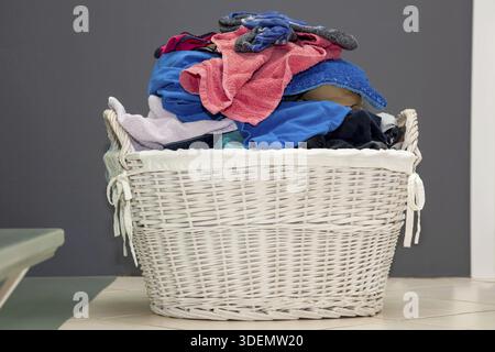Wooden basket with dirty laundry on floor. Clothes in rattan basket. multicolored dirty laundry ready for washing Stock Photo