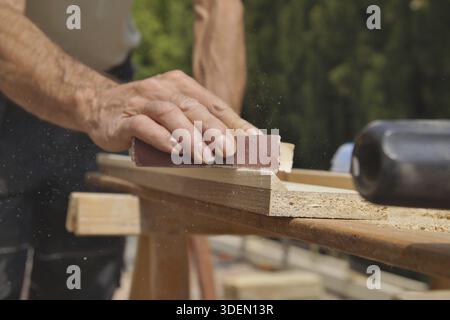 Male worker hands smoothing wood board using sandpaper. Sanding wood plank. detail, old carpenter hands at work with sand paper Stock Photo