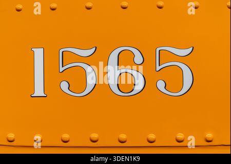 White numerals 1565 painted on an orange metal surface with visible rivets Stock Photo