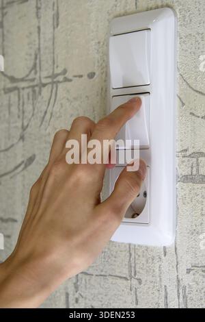 Female hand on white light switch key Stock Photo