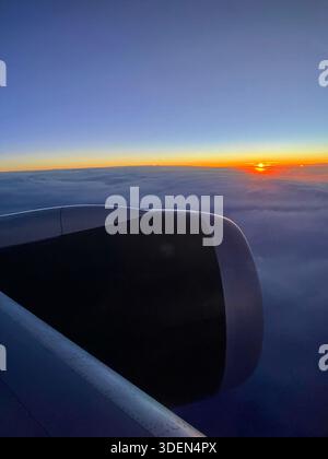 Airplane Window View Clouds Sunrise Sunset.The view from an airplane window looking over wing and engine. Clouds and sunrise sunset outside. Stock Photo