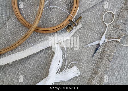 Set for embroidery, garment needle, thread, scissors and embroidery hoop on unbleached linen fabric. Top view Stock Photo