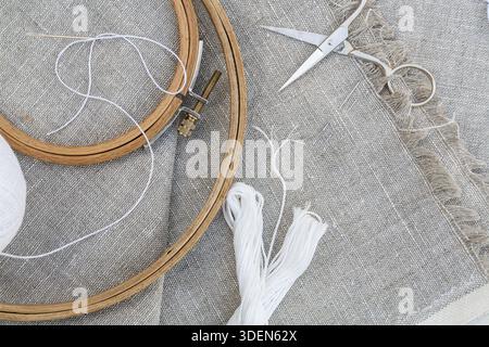 Set for embroidery, garment needle, thread, scissors and embroidery hoop on unbleached linen fabric. Top view Stock Photo
