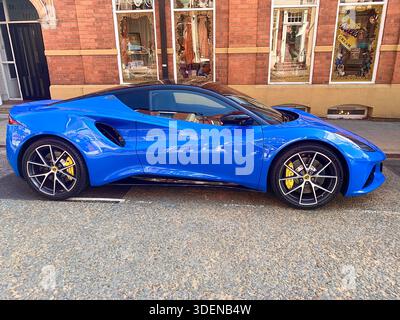 A vibrant blue sports car with black accents and yellow brake callipers parked on a street in front of a traditional red brick building classic  car Stock Photo