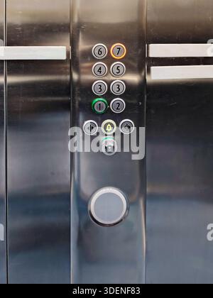 A detailed view of a stainless steel elevator button panel in an office building. The panel shows numbered buttons, an illuminated 7th floor indicator Stock Photo