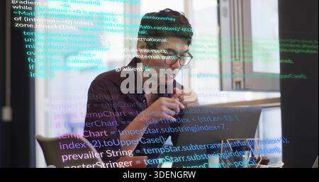 Typing Asian man wearing dark shirt, glasses at modern office with laptop, coffee, reflected code Stock Photo