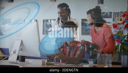Collaborating three colleagues pointing at desktop in creative office, coral sweater, DSLR camera Stock Photo
