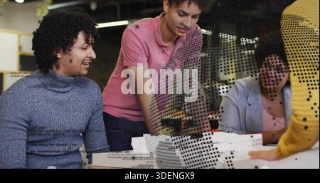 Collaborating group in studio attire arranging white models and foam mockups, patterned screen Stock Photo