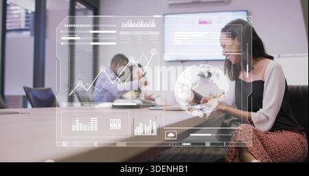Tapping tablet, woman in white blouse presenting data overlay on wall screen at table, copy space Stock Photo