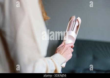 Female hand with electric hair curler in cozy interior symbolizing home beauty care and personal grooming concept Stock Photo