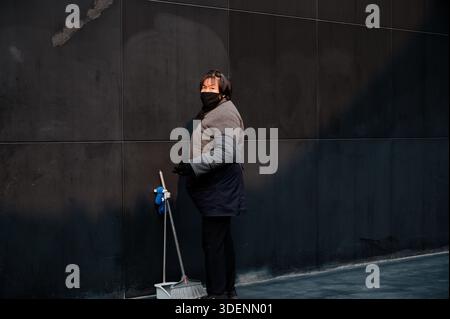 Masked cleaner pausing with her broom against a dark wall at Unique Henan: Land of Drama Stock Photo
