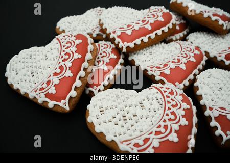 Heart shaped gingerbread cookies featuring intricate white royal icing designs on a dark background. Stock Photo