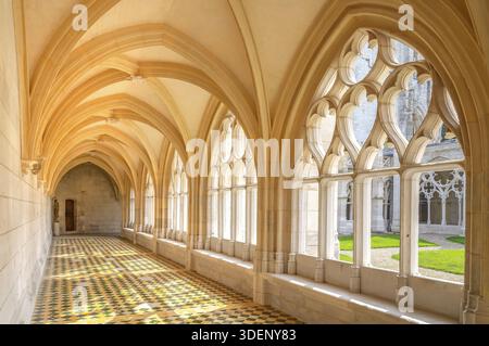 Light-flooded gallery in the cloister of Saint-Wandrille Abbey with a focus on the magnificent flamboyant-style window arches, whose delicate tracery Stock Photo