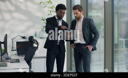 Two diversity businessmen talking in office using modern digital tablet together talk multiethnic business men male co-workers discussing online Stock Photo
