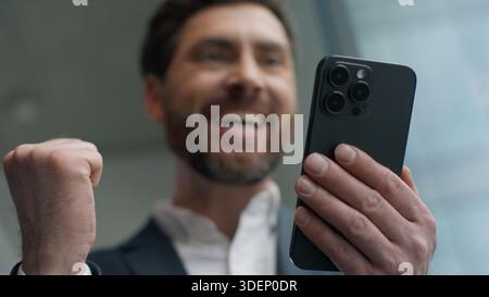 Caucasian male businessman business man in office excited celebrating success with smartphone happy rejoicing good news receiving mobile phone message Stock Photo