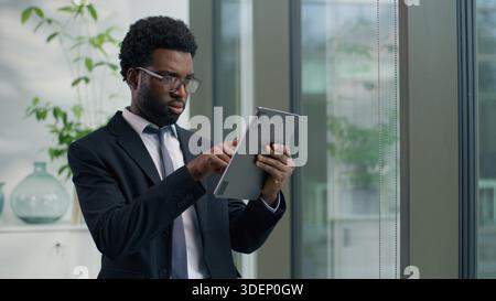 Concentrated focused African American businessman in office using digital tablet analyze data project with wireless computer technology business man Stock Photo