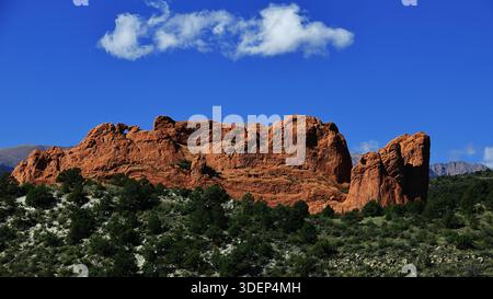 Panoramic red rock ridge with a small natural window at Garden of the Gods Park, Colorado Springs, Colorado, USA, with mountains and white clouds. Stock Photo