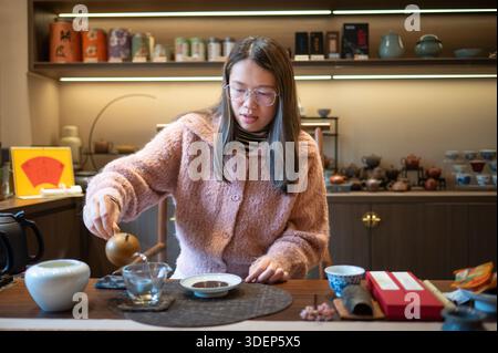 Asian woman pours tea from a teapot into a stylish teacup, showcasing the graceful act of preparing for a tea gathering and traditional Chinese tea ce Stock Photo
