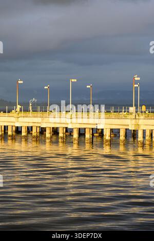 Warm evening glowing light on concrete pier reflecting in calm sea water Stock Photo
