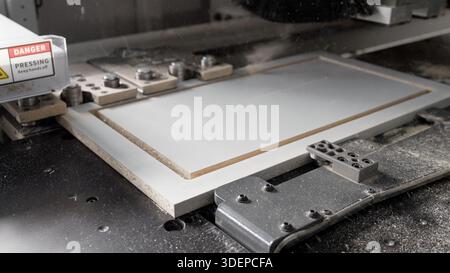 Cnc router cutting a white mdf board, creating precise grooves for cabinet making in an automated woodworking factory Stock Photo