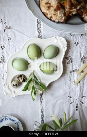 Italian Easter table setting. Natural dyed eggs in green color and quail eggs. Vintage tablecloth. Stock Photo