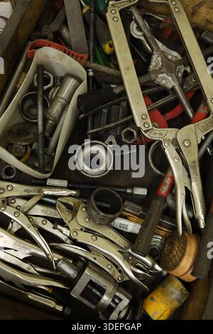A top-down perspective of a messy toolbox or drawer containing various mechanical hand tools, locking pliers (vice-grips), bolts, and metal parts in a Stock Photo