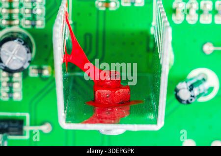 Close-up of a red bolt and thermal paste on a green circuit board with components Stock Photo