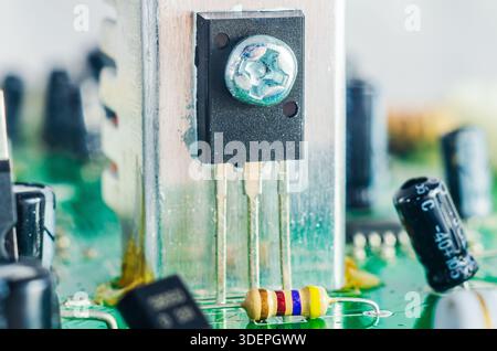 Close-up macro shot of electronic components on a green circuit board with a transistor and resistor Stock Photo