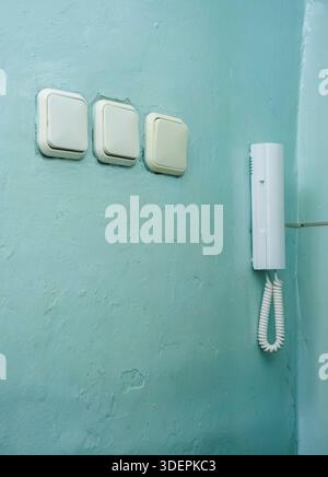 Three light switches and an old white wired intercom are mounted on a worn, textured aqua colored wall, showing everyday functional elements in a resi Stock Photo