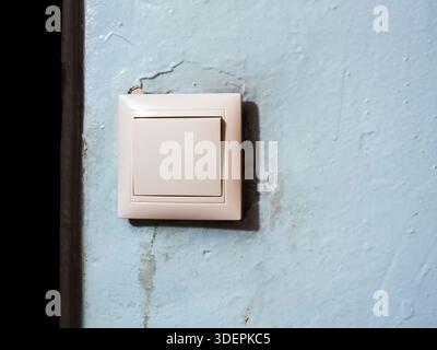 Light switch mounted on cracked, peeling blue wall showing wear, decay and exposed wiring  symbolizing household electricity, repair, maintenance and Stock Photo