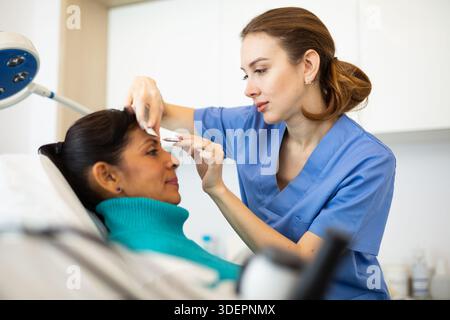 Beautician using white pencil and ruler for marking skin of latin woman Stock Photo