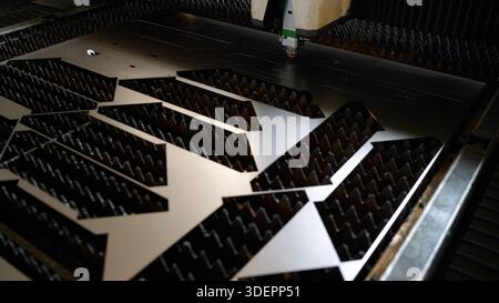 Laser cutting machine processing a metal sheet with precision, showing parts being cut from the surface in an industrial setting Stock Photo