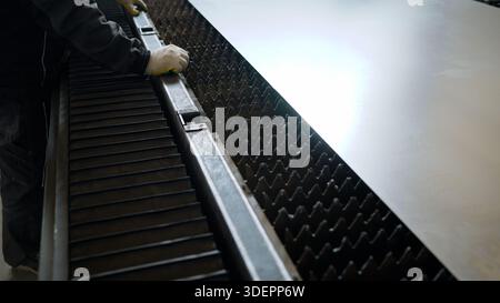 Worker wearing protective gloves loading a stainless steel sheet onto the bed of a cnc laser cutting machine in a factory Stock Photo