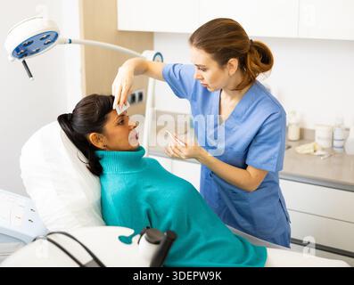Beautician using white pencil and ruler for marking skin of latin woman Stock Photo