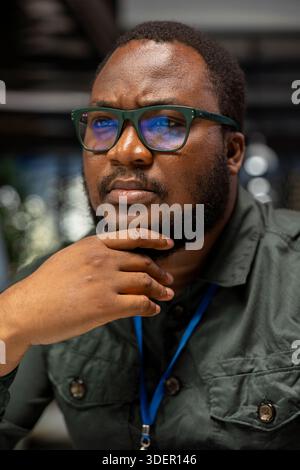 Black general manager envisioning rational solution and scratching his chin, works after hours at desk. Man engaging in critical thinking, evaluating each option for a different perspective. Stock Photo
