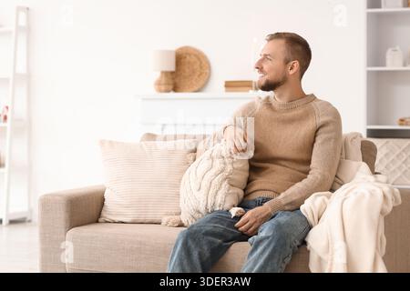 Young man in beige sweater sitting on sofa at home Stock Photo