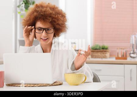 Redhead female freelancer in bathrobe working with laptop at home Stock Photo