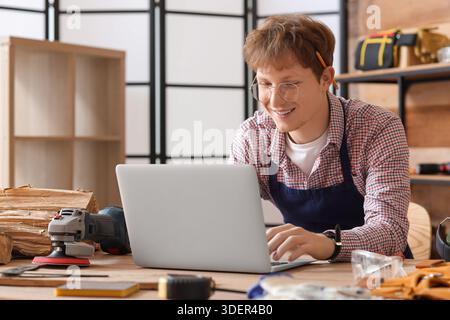 Young carpenter using laptop at table in workshop Stock Photo