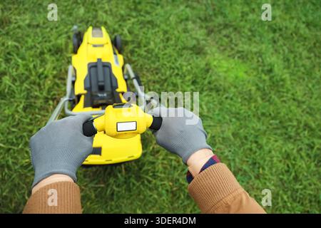 Male hands using modern lawn mower outdoors, top view Stock Photo