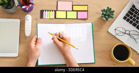 Man with stationery writing in notebook on table in office, top view Stock Photo