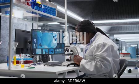 Black scientist examining samples under microscope in a modern laboratory. Research work integrates biotechnology, molecular science and advanced diagnostics to shape medical discovery. Stock Photo