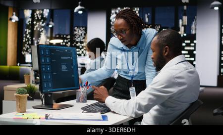 Black IT engineers team developing app and software algorithm on pc, working in the office late at night. Specialists use digital tools and focuses on script engineering and coding. Stock Photo