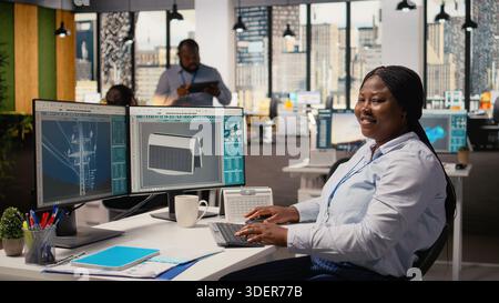 Happy product developer in office using advanced solar cell technology to create sustainable energy based device. Smiling RD expert tests solar panel lamp prototype to maximize power output, camera A Stock Photo