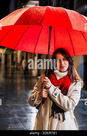 Woman holding red umbrella walking city street in rain Stock Photo