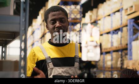 Coworkers collaborating on a live stream in storage room warehouse, showcasing parcel handling and order processing. African American workers present goods for a commercial campaign. Camera B. Stock Photo