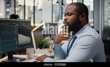 Close up of trader analyzing stock exchange analytics, doing thinking, evaluating trading strategy in prop firm office. African american man brainstorming, assesses risk in financial markets Stock Photo