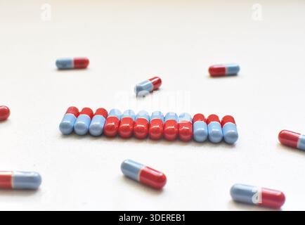 Red and blue capsules in a row and scattered on a white table, medical concept, healthcare, prescription medication, pharmaceutical still life. Stock Photo