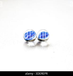 Two glass marbles with blue centers on a white table, close-up still life with clean minimal background, simple composition and calm mood. Stock Photo