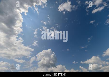 A stunning view of a bright blue sky adorned with fluffy white clouds and radiant sunlight shining through Stock Photo