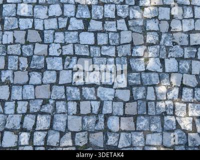Cobbled stone surface with paving pattern. Textured ground and roadway material creating historic urban path. Weathered antique design with rough rock Stock Photo